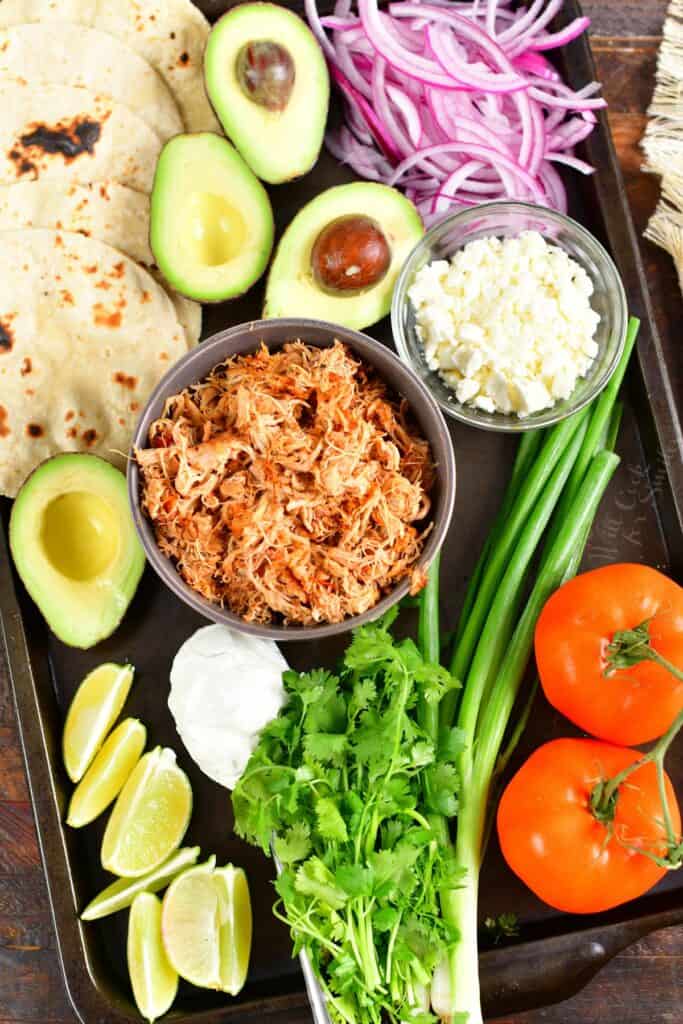 shredded chicken and toppings to make tacos laid out on a sheet pan