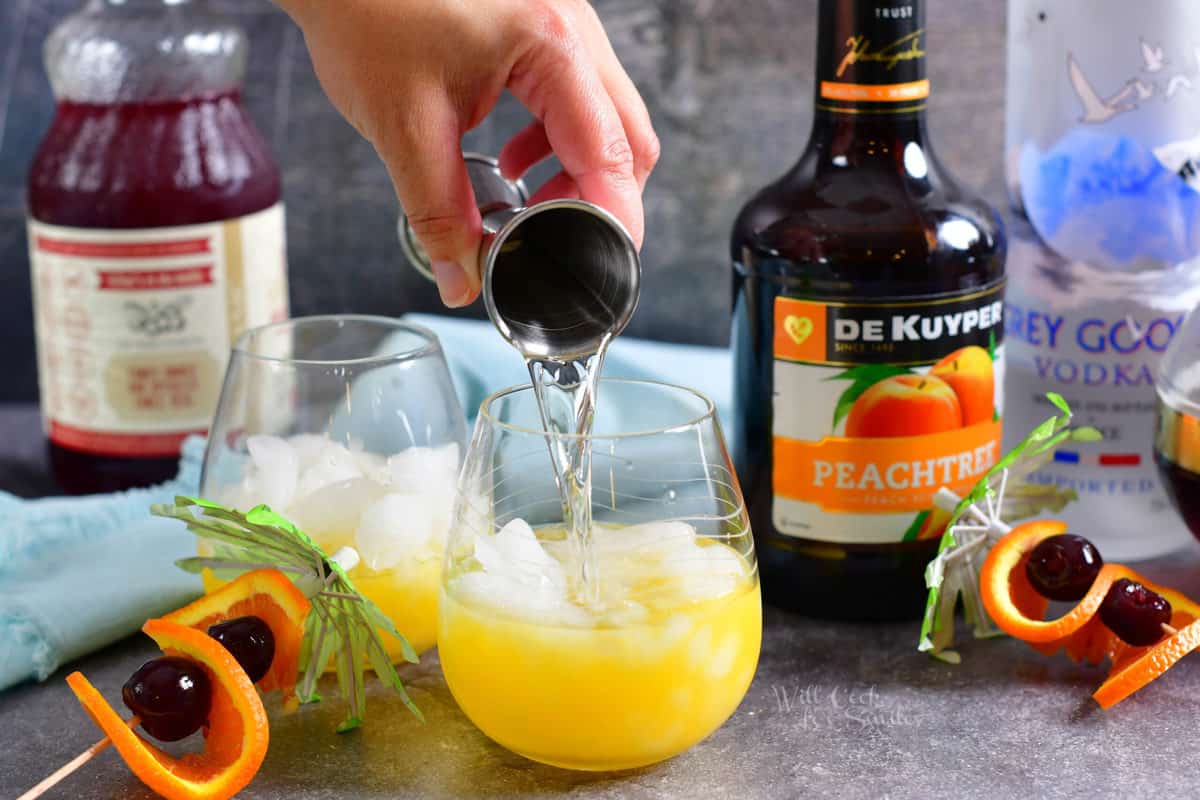 Vodka is being poured on top of the ice and orange juice.