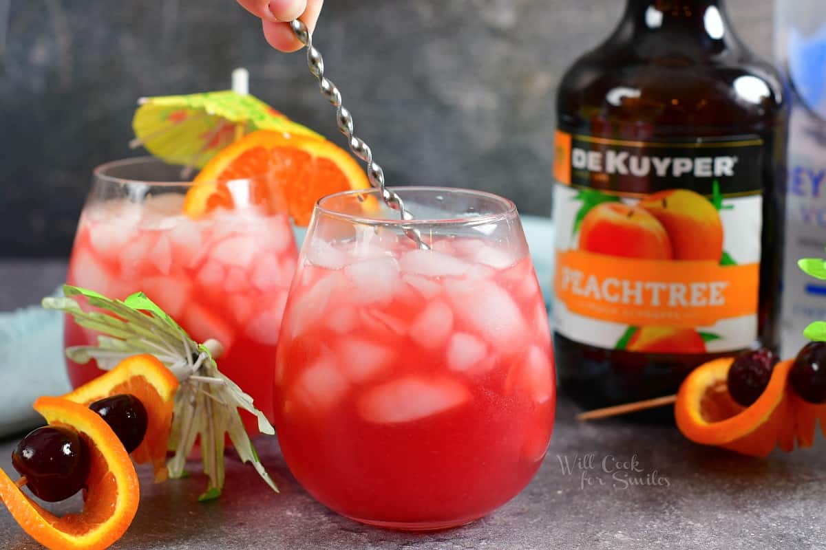 A small spoon is stirring a cocktail in a glass.