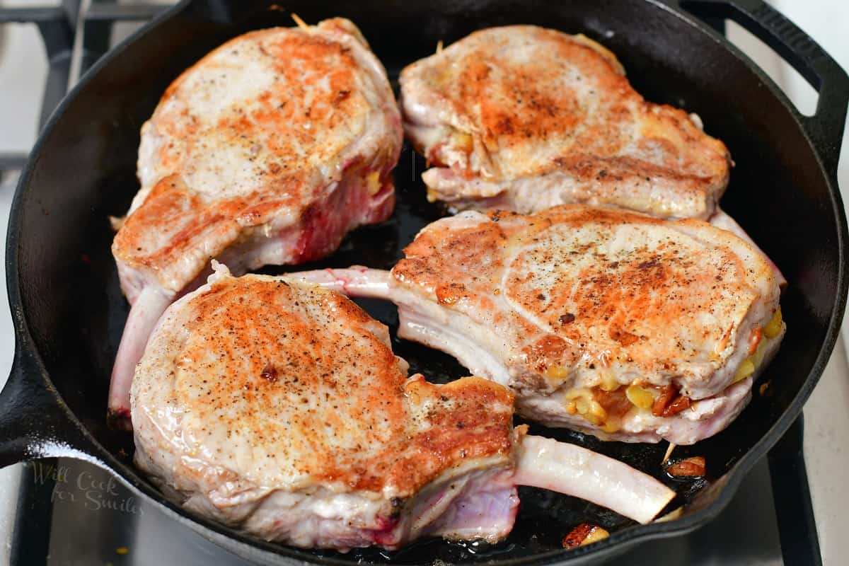 Pork chops are browning as they cook in a pan.