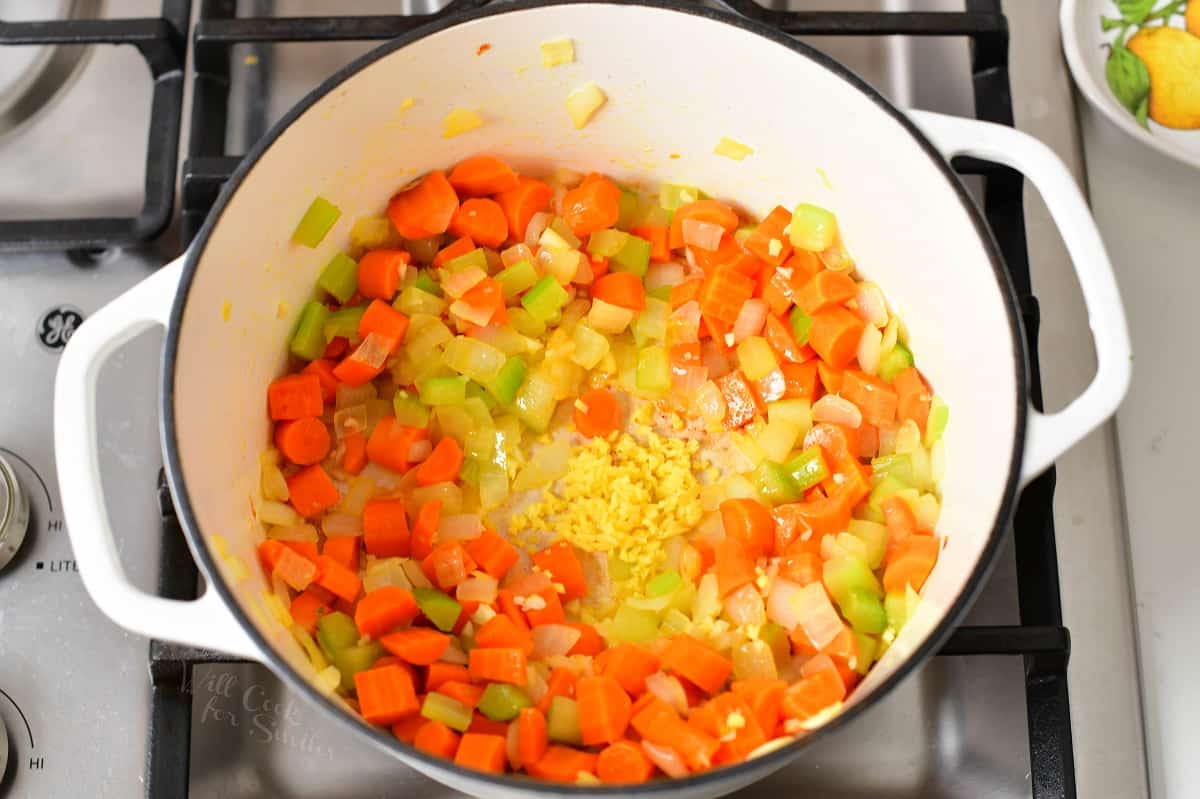 adding garlic to the sautéing vegetables in a pot.
