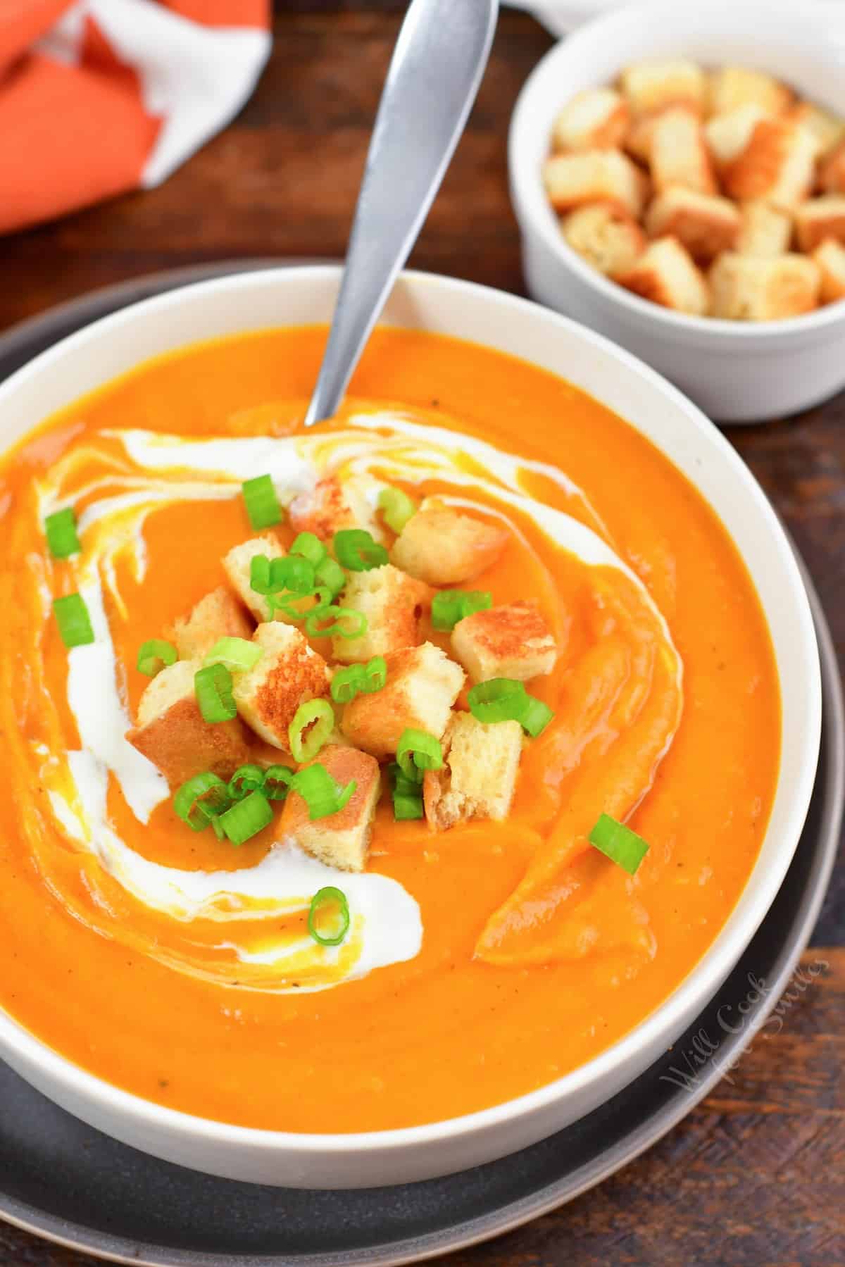 a large bowl of sweet potato soup in a bowl with croutons, sour cream swirl, and green onion.