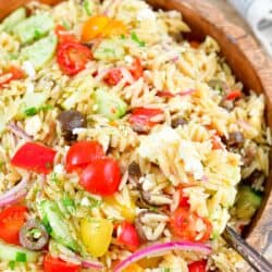 scooping out orzo salad from a wooden bowl