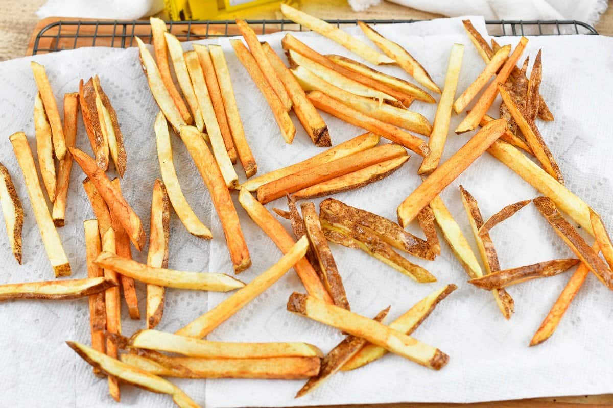 cooked thin and crispy golden fries spread out on the paper towels