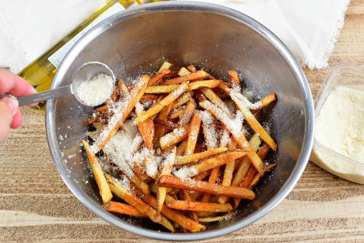 adding Parmesan cheese to cooked golden fried fries in a bowl.