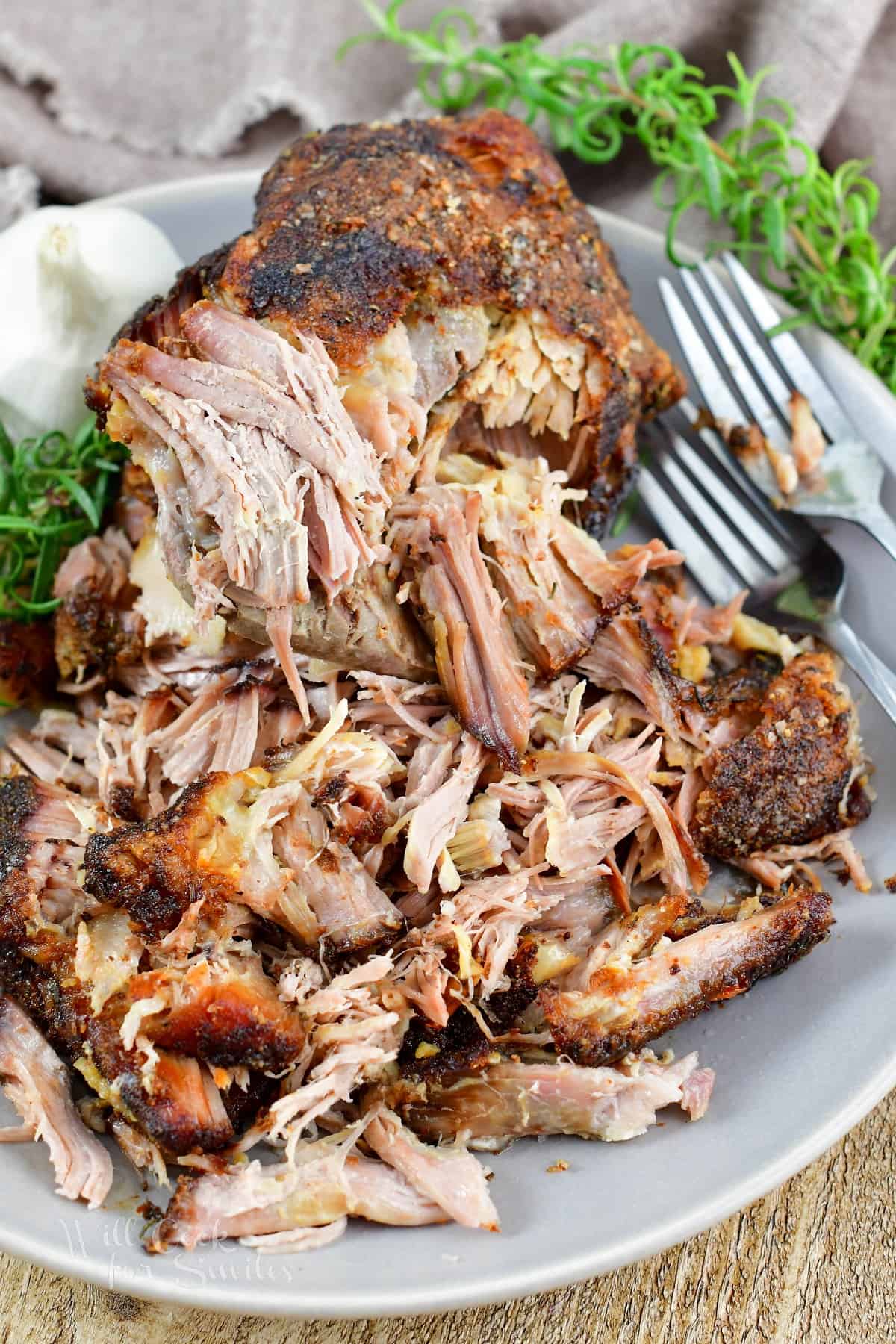 large piece of pork and pulled pork in the plate with forks and rosemary.