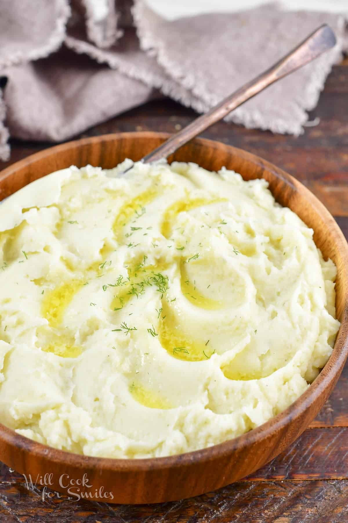 smooth and fluffy mashed potatoes with butter and a spoon in a wooden bowl.