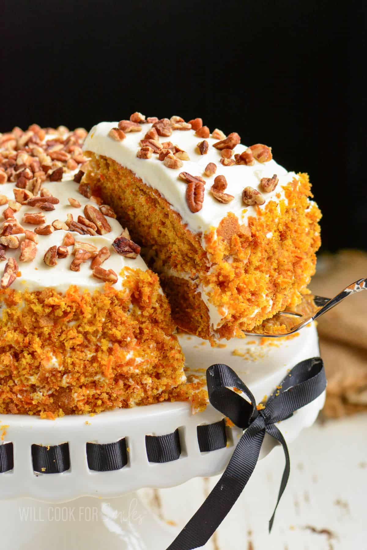 taking out a sliced of carrot take sitting on a cake stand with ribbon.