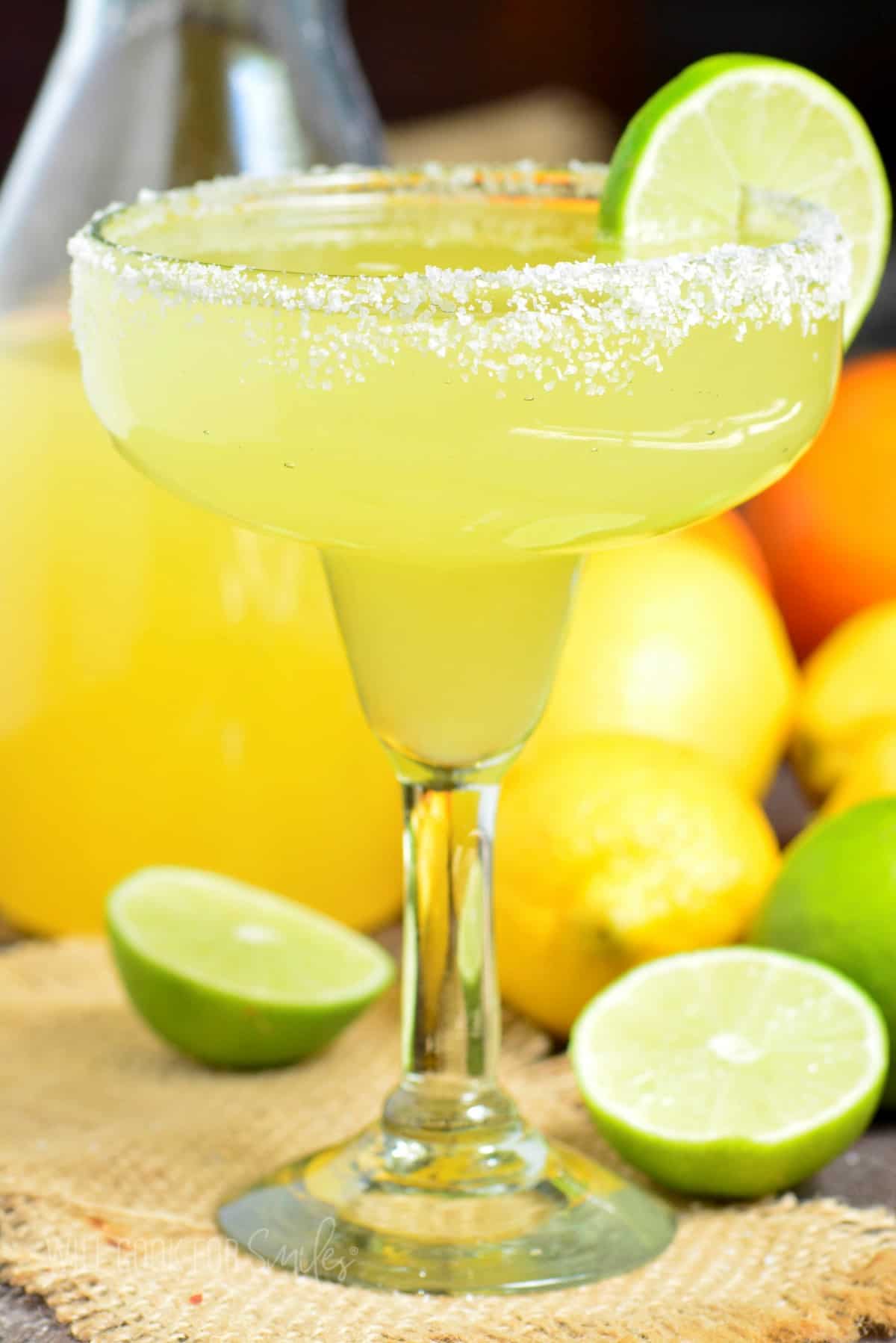 full view of a margarita glass filled with cocktail, salted rim, and lime on side.