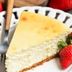 slice of classic cheesecake on a white plate with a fork and a strawberry.