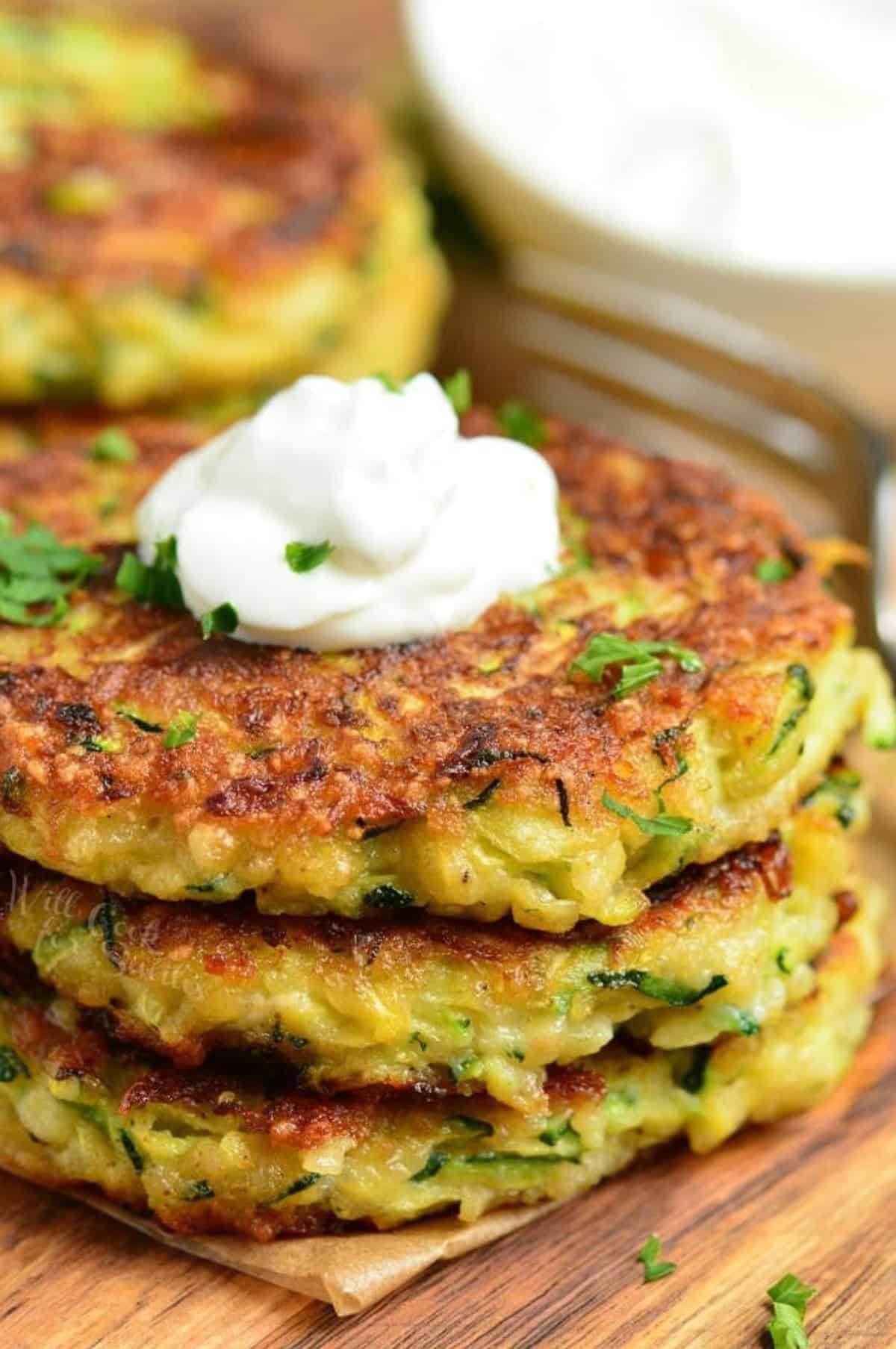 three zucchini fritters stacked and topped with sour cream.