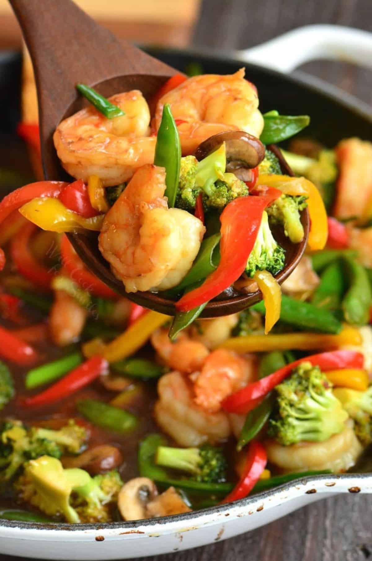 scooping out some shrimp stir fry with a large wooden spoon from the skillet.
