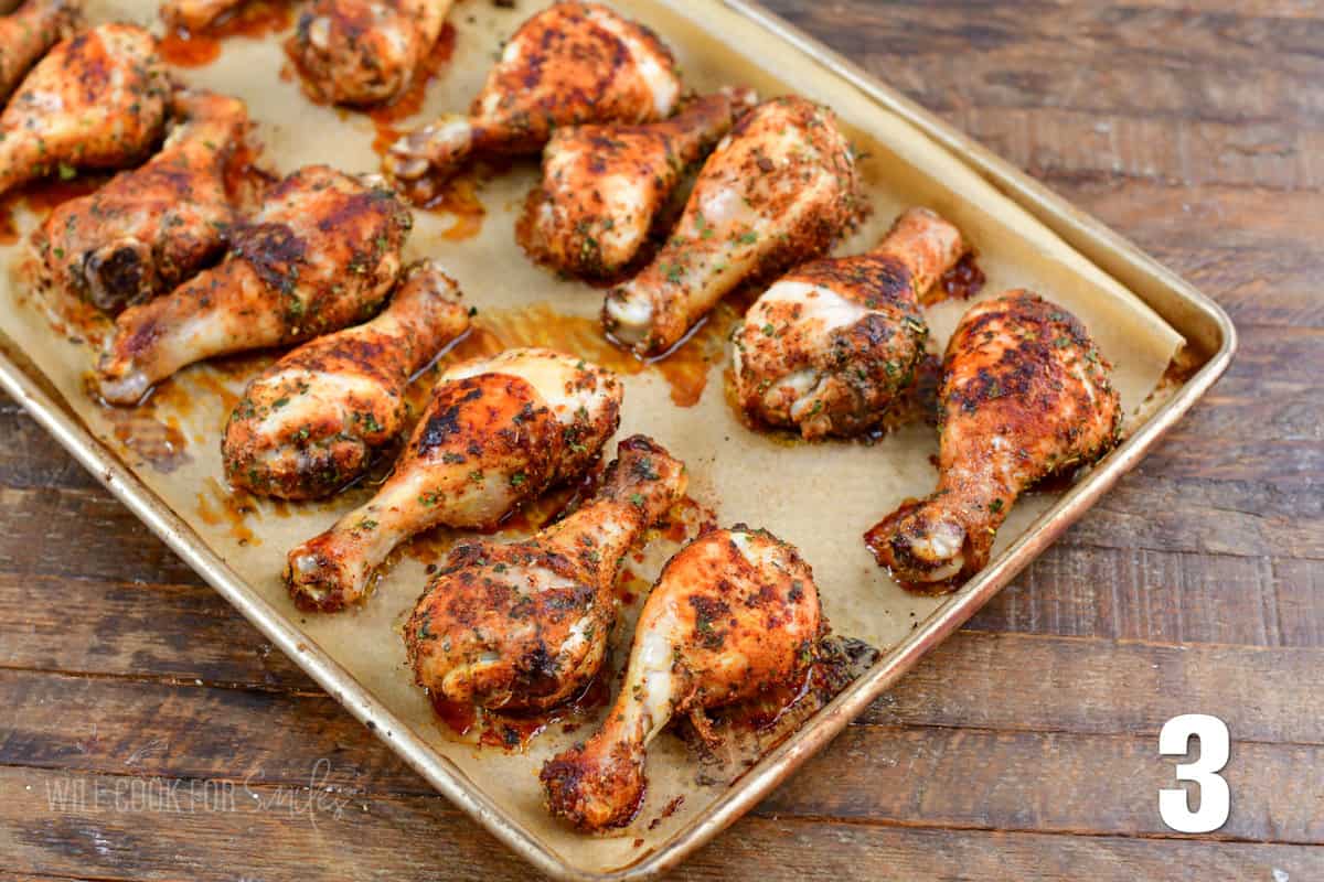 A baking sheet is lined with parchment paper and baked chicken drumsticks.