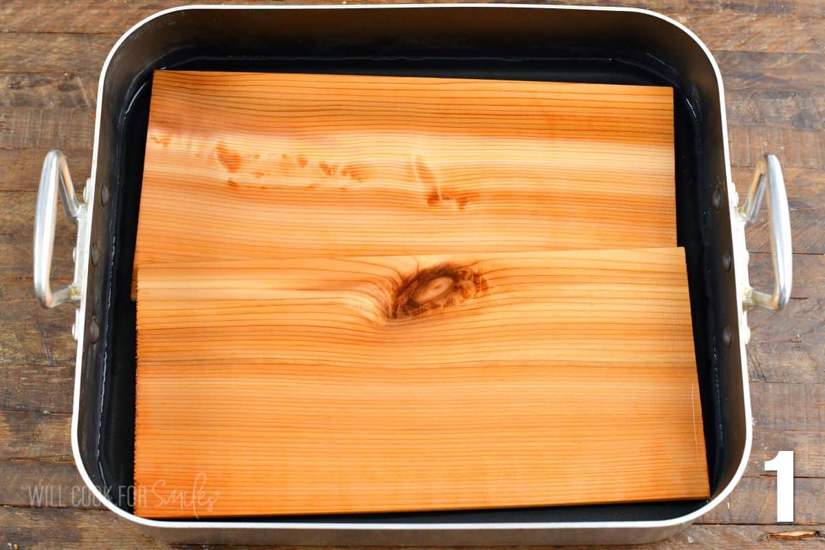 Two cedar planks are soaking in water a large roasting pan.