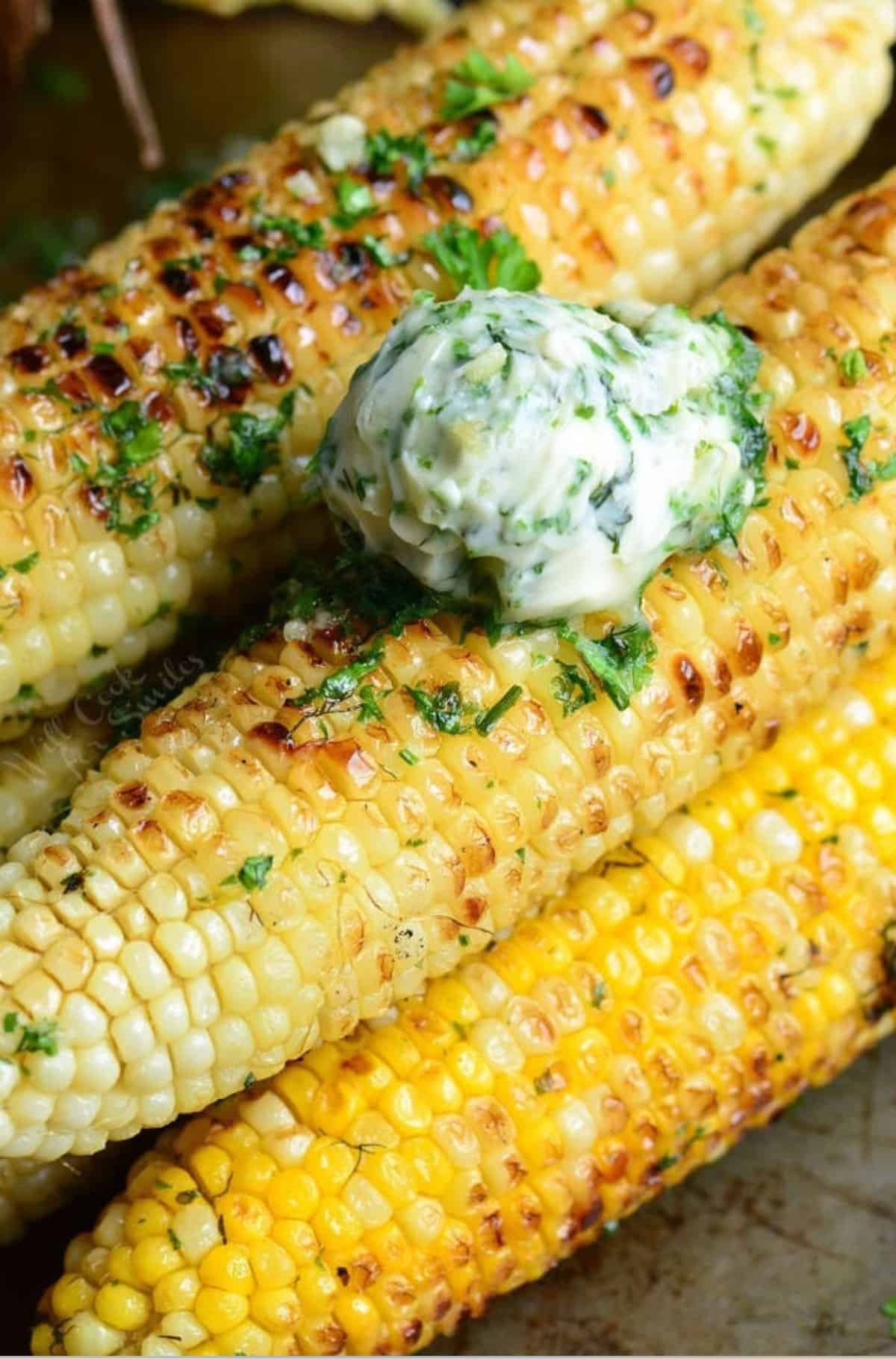 several stacked grilled corn on the cob and topped with a scoop of garlic butter.