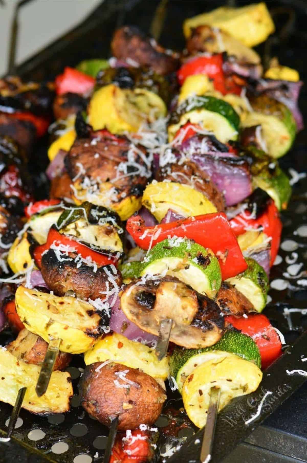 five long skewers with mixed Italian grilled vegetables on them.