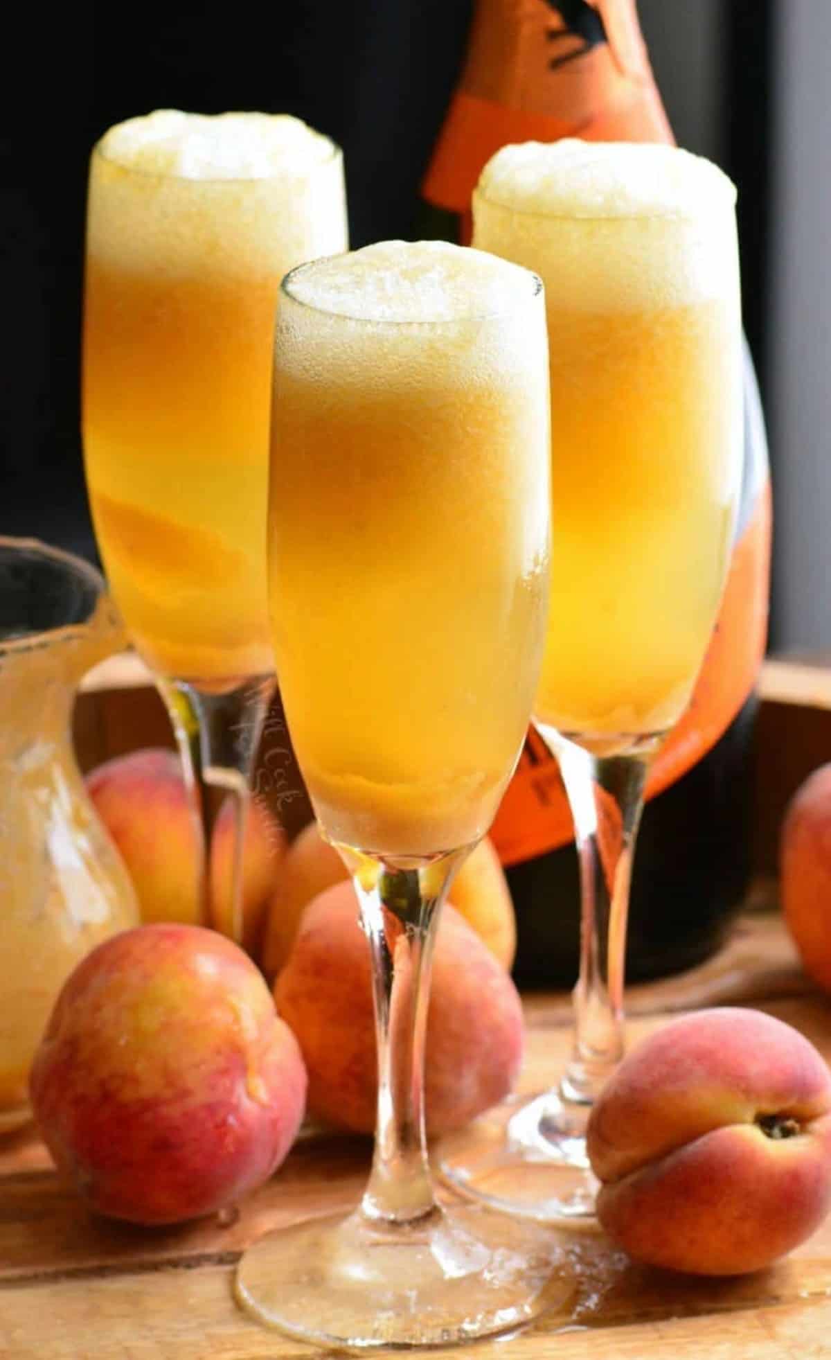 three tall champagne glasses filled with orange peach cocktail and bottle of prosecco.