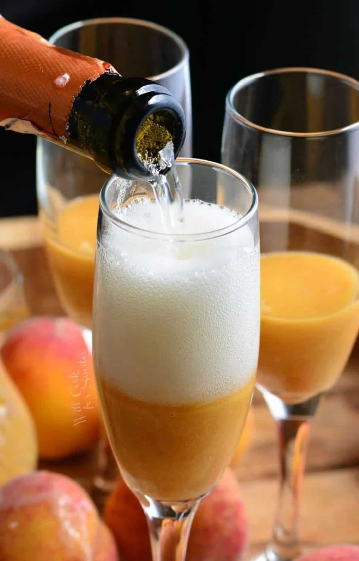 pouring prosecco into the champagne flute with fresh peach puree in it.