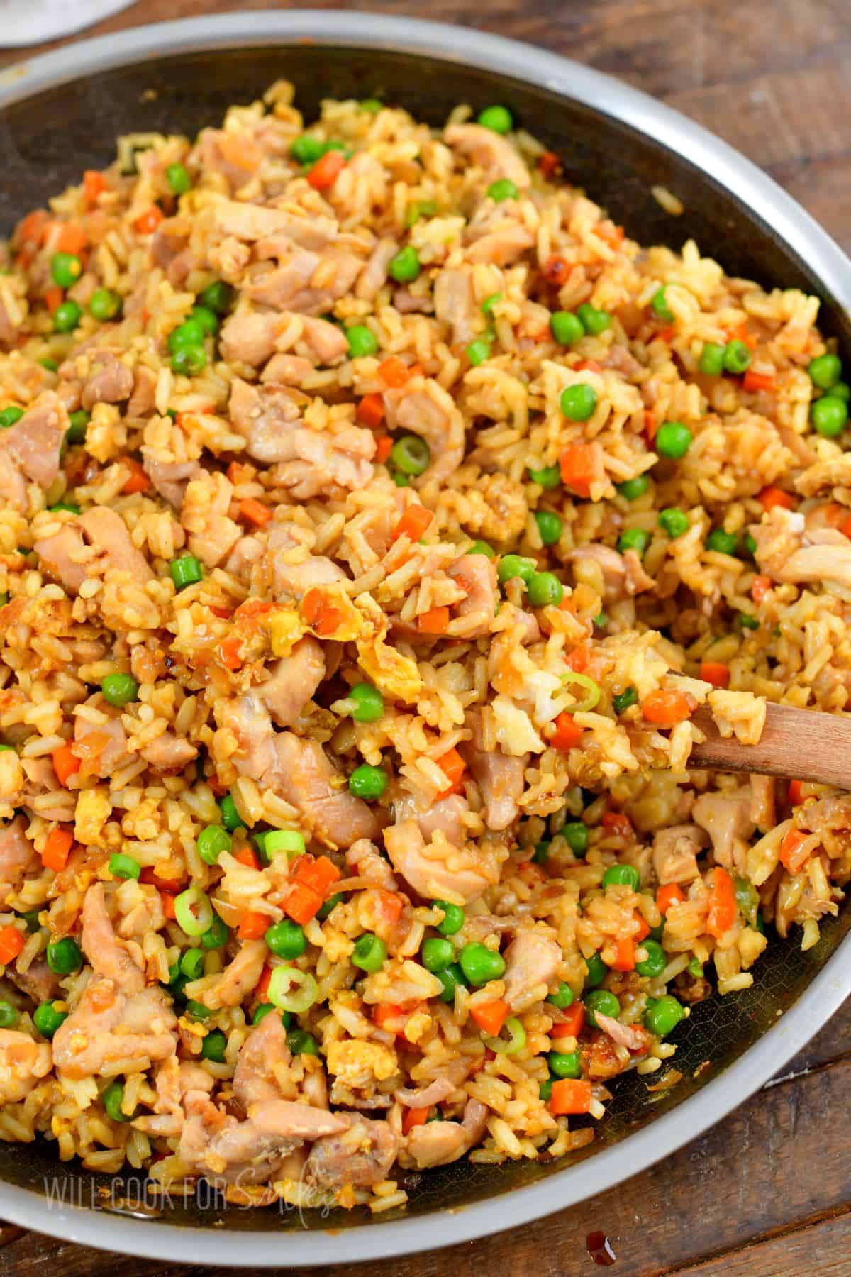 chicken fried rice in a cooking pan with some scooped on a wooden spoon.