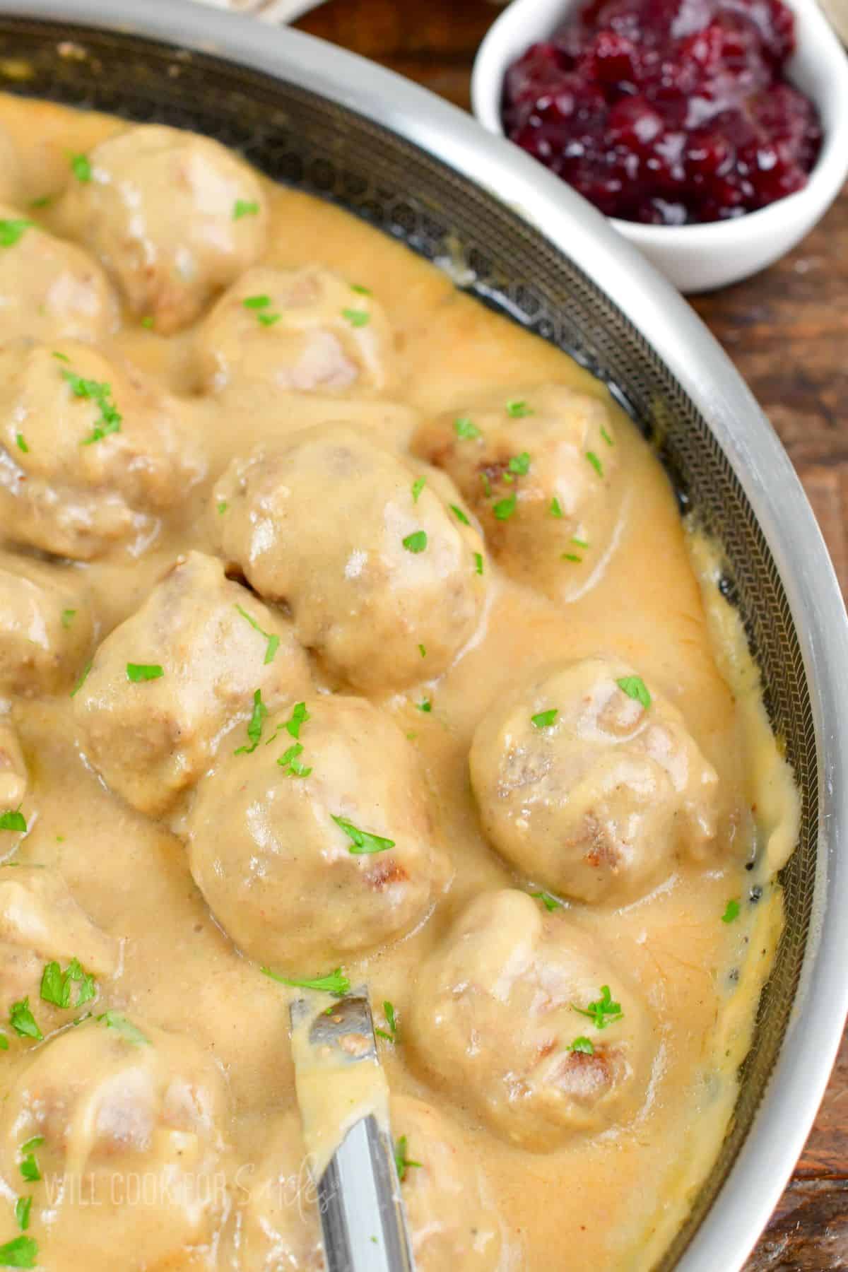 several meatballs in creamy gravy in the pan with a metal spoon.