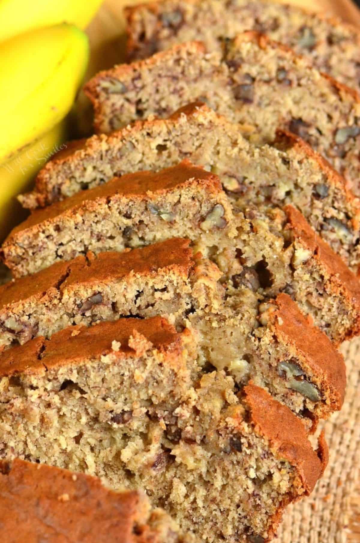 Several slices of banana bread are lined up next to bananas.