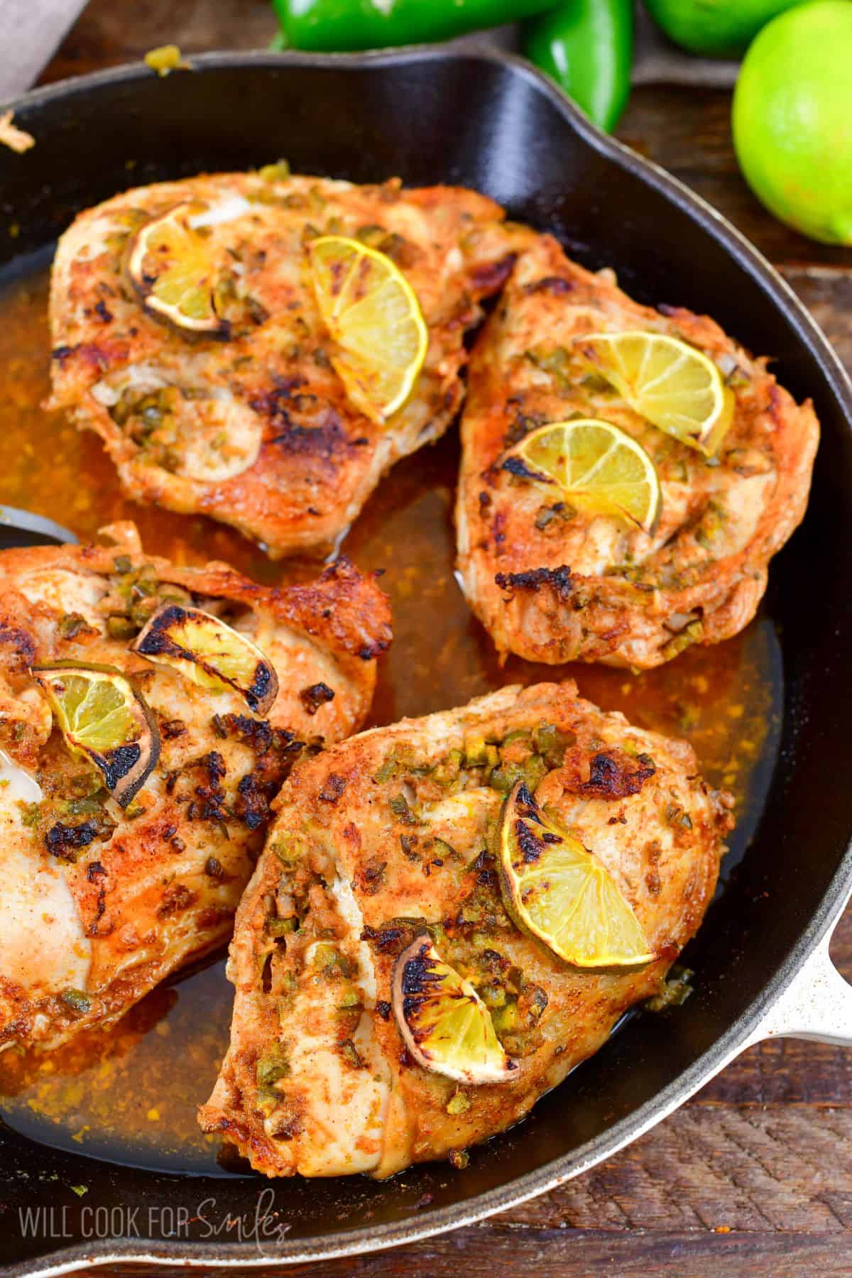 Charred pieces of lemon are placed on top of chicken breasts in a skillet.