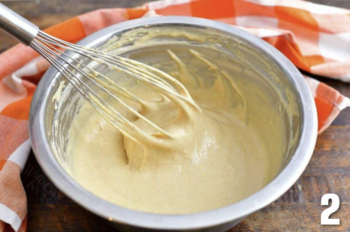 whisking pancake batter in the metal bowl with a whisk.