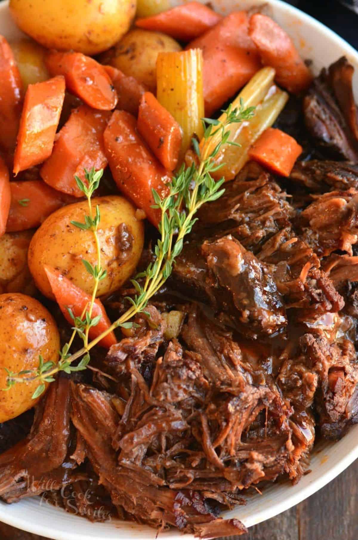 Pot roast with carrots and potatoes and a sprig of thyme in a bowl.