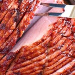 baked ham on a cutting board with a fork pulling the sliced pieces apart.