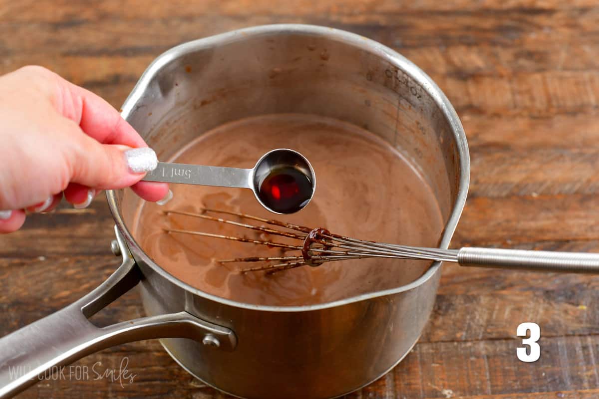 adding vanilla to the pot that is sitting on a wood surface.