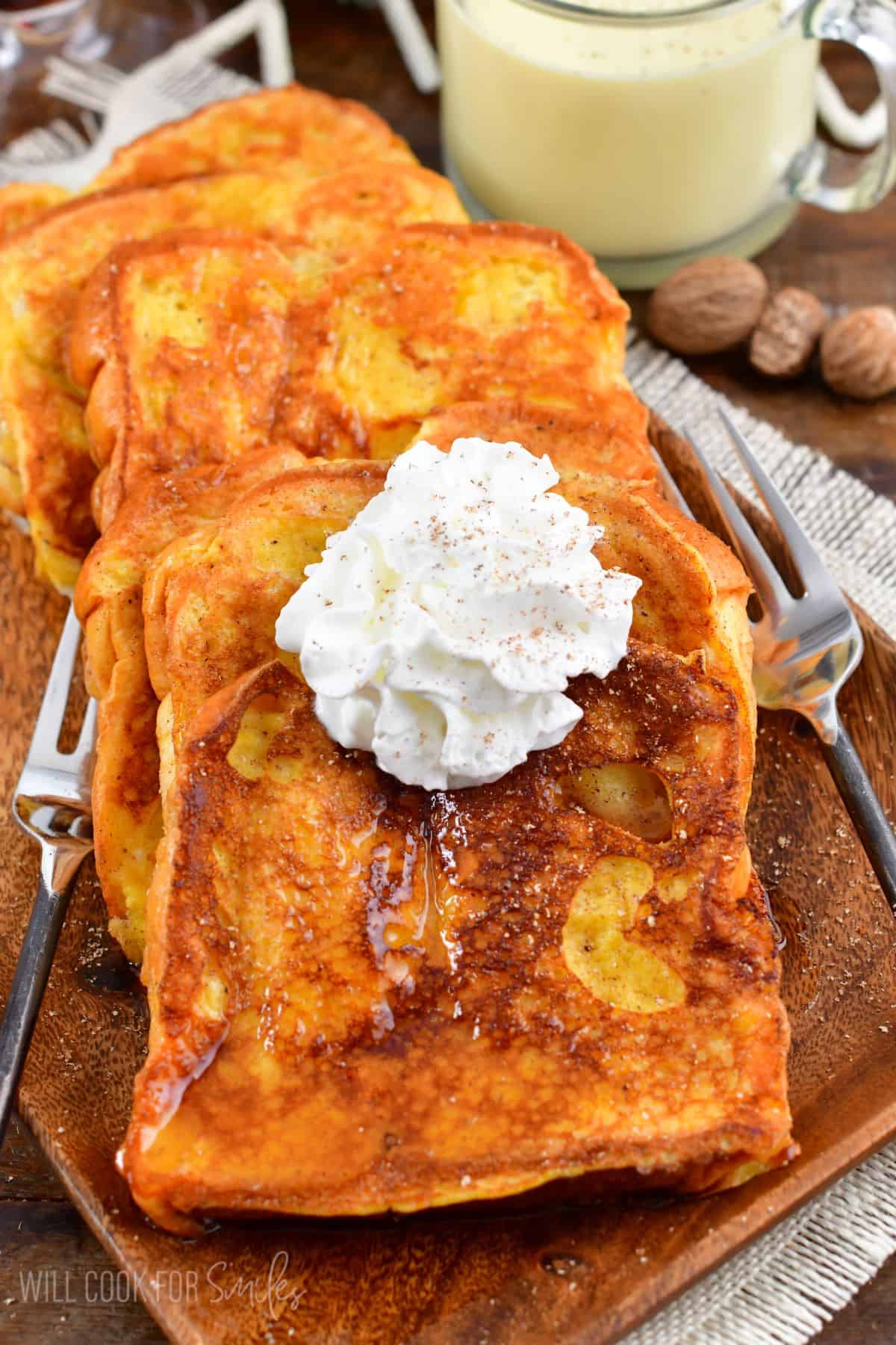 Soft and golden Eggnog French Toast stacked on a plate with whipped cream on top and dusting of nutmeg.