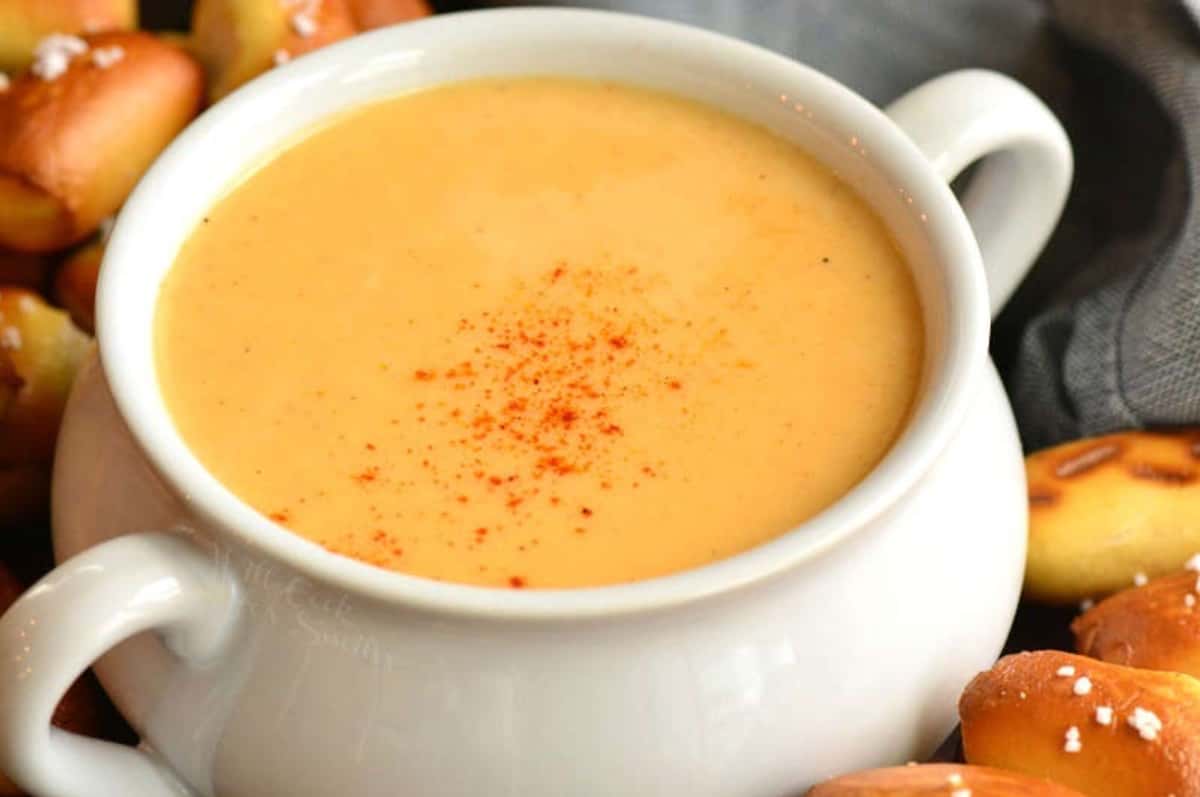 beer cheese dip topped with some paprika and pretzel bites around.