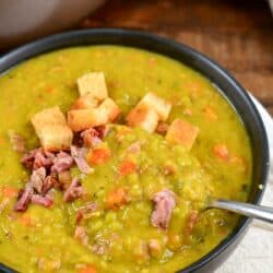 split pea soup in a bowl topped with croutons and ham with a spoon.