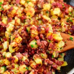 Corned beef hash in a pn with a wooden spatchula scooping some up.