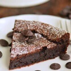 slice of flourless chocolate cake on the plate with some chocolate chips around.