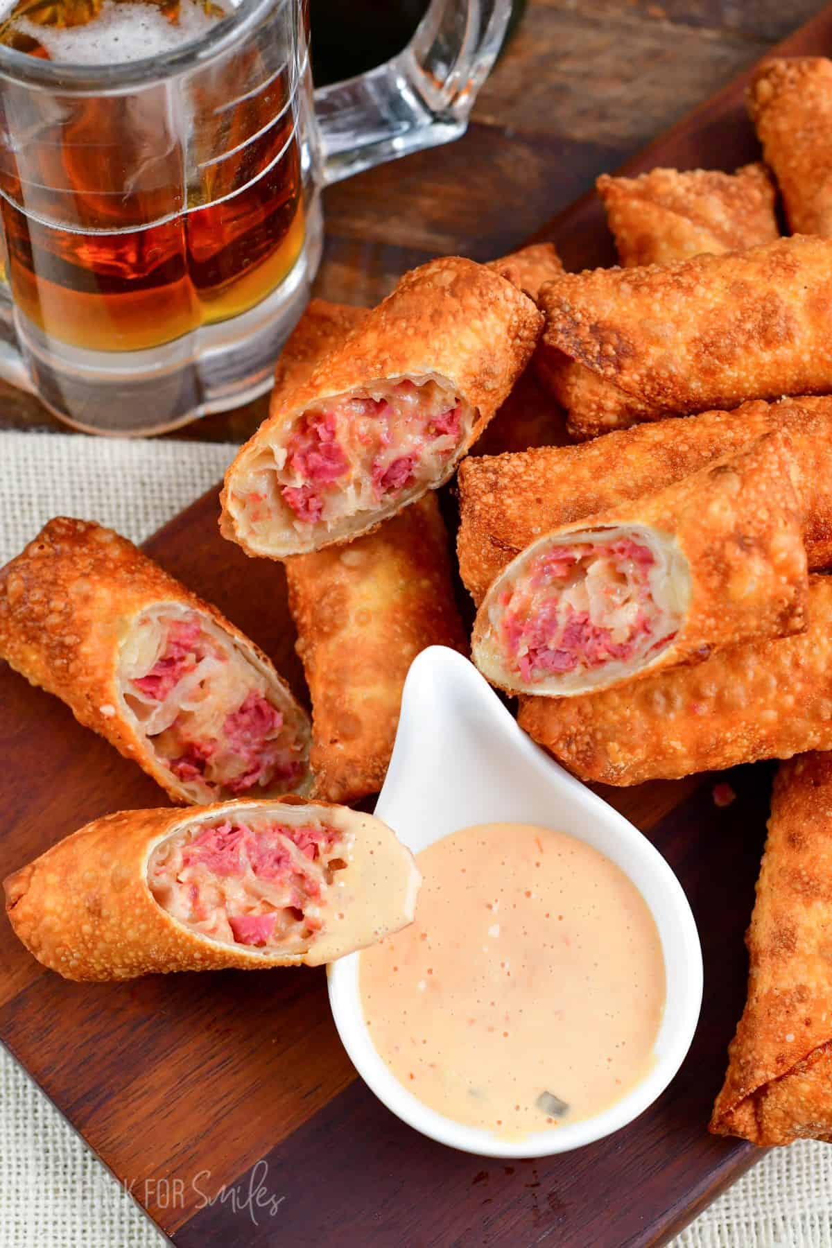 wood tray with eggrolls several have been cut in half with a small bowl of dressing.