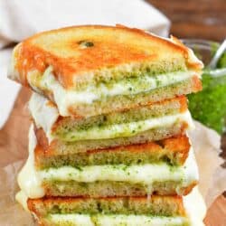 two pesto grilled cheese sandwiches cut in half and stacked up on a piece of parchment paper.