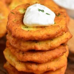 stacked of potato pancakes with a dollop of sour cream on top on a wood surface.