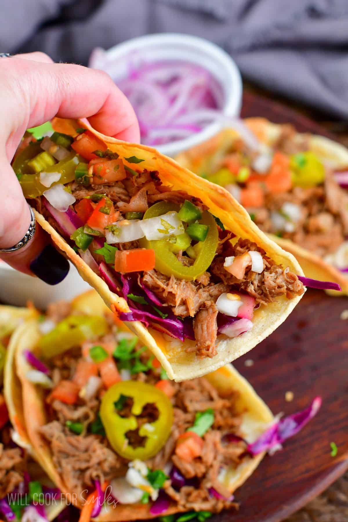 Holding a pork taco up with the other pork tacos in the bakcground.