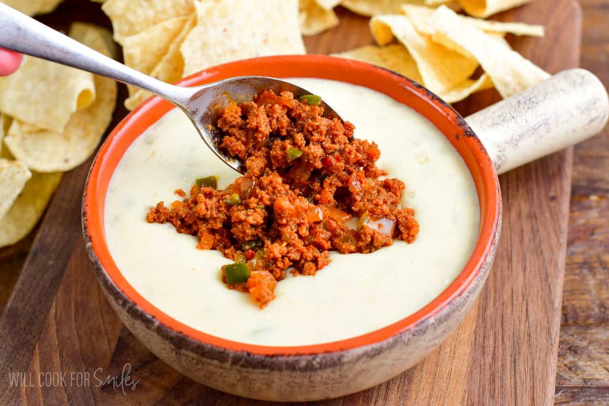 adding cooked chorizo and veggies on top of the bowl of queso blanco.