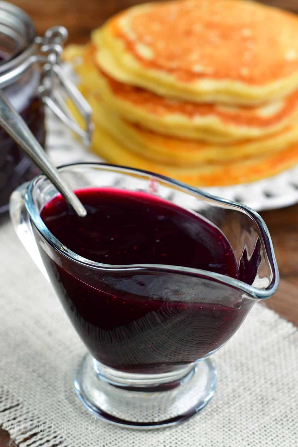 blueberry syrup in a saucer with a spoon on a white table runner.
