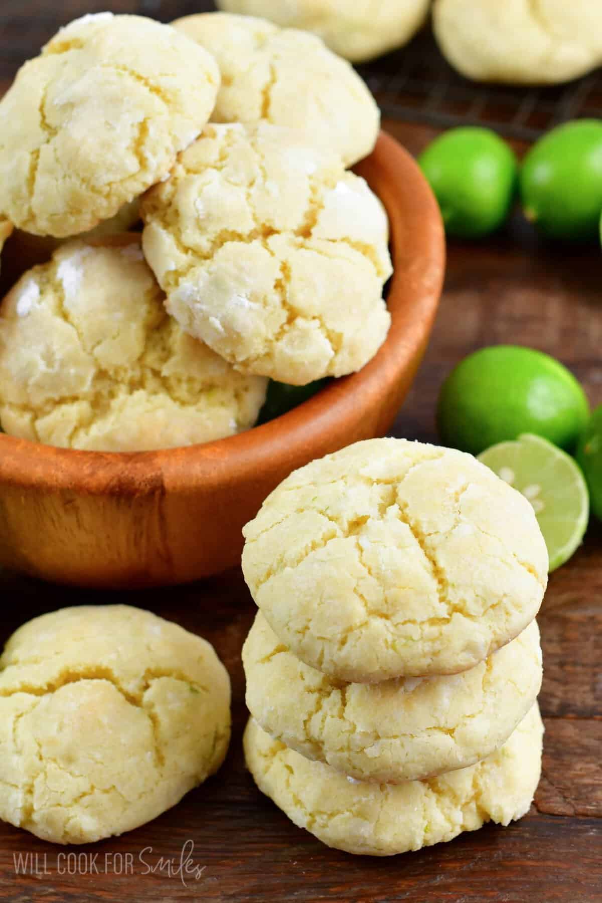 Cookies stacked in a wood bowl with a stack of cookies and limes beside the bowl.