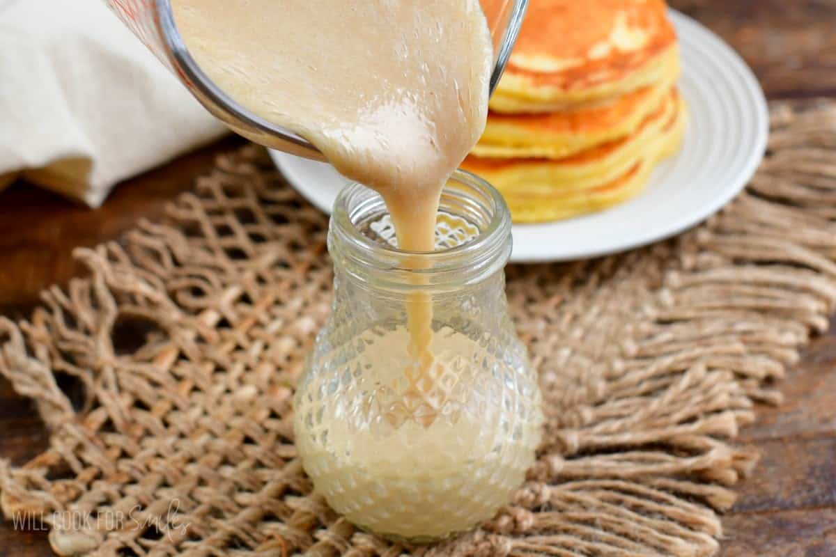 pouring coconut syrup into a glass jar that is on a burlap placemat.