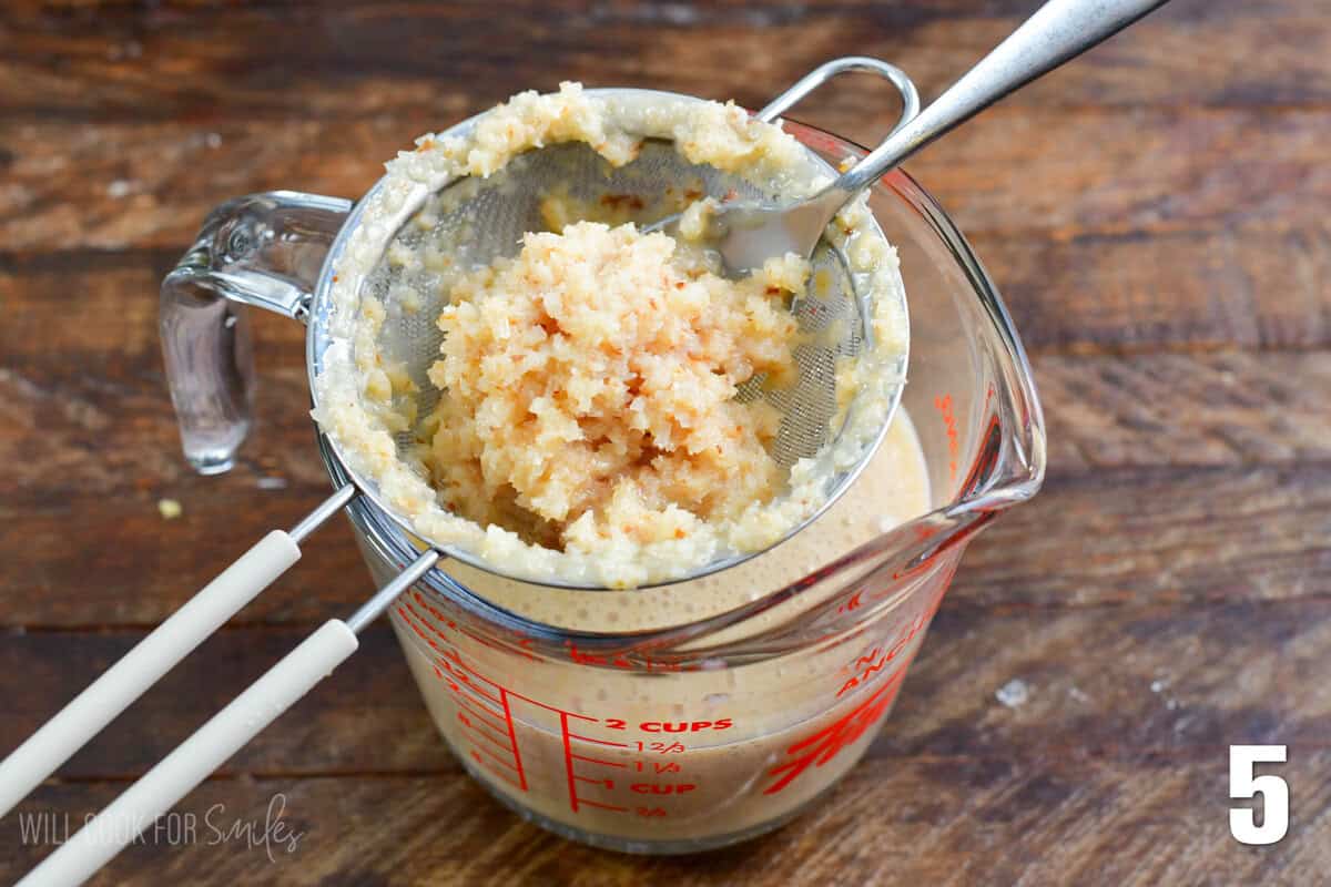 Straining the coconut in a small mesh strainer into a measuring cup.