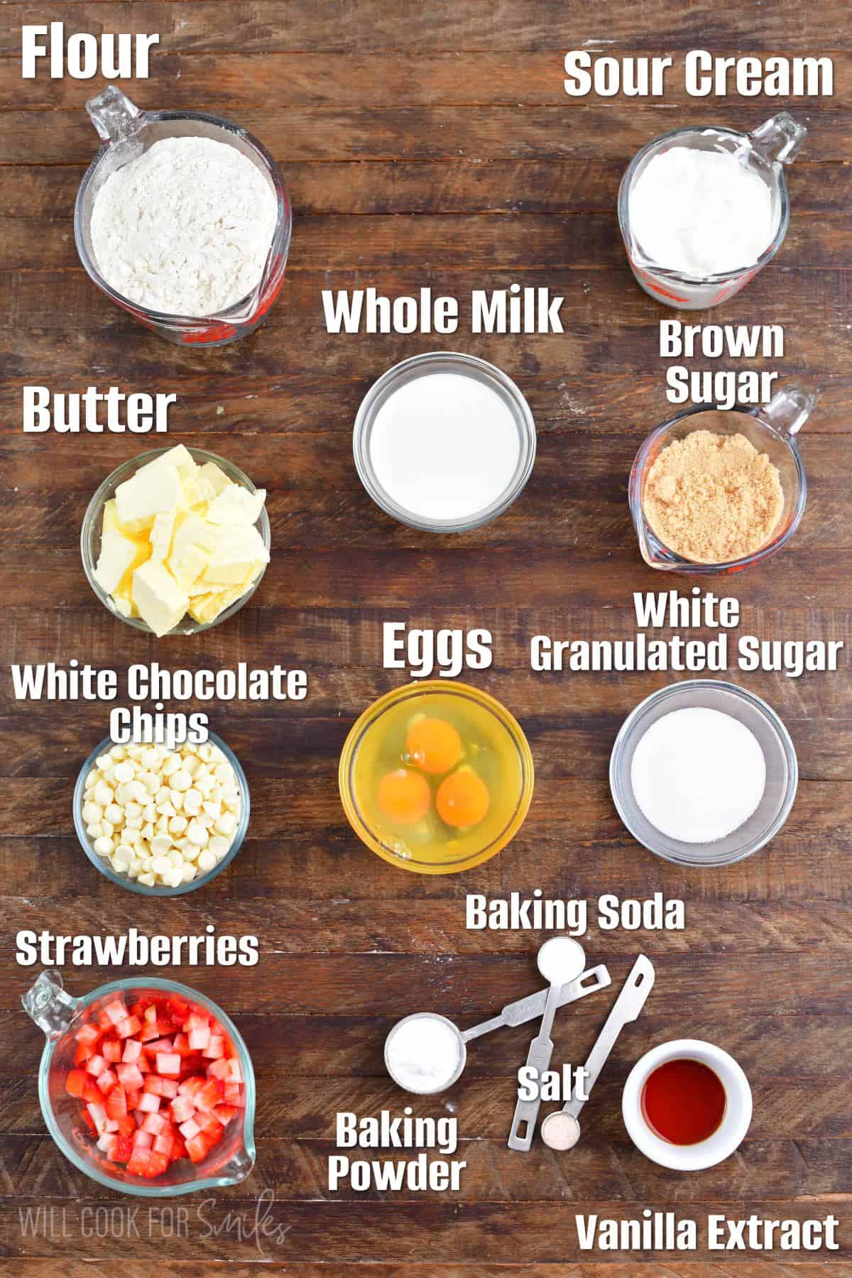 Labeled ingredients for white chocolate chip strawberry muffins on a wood surface.