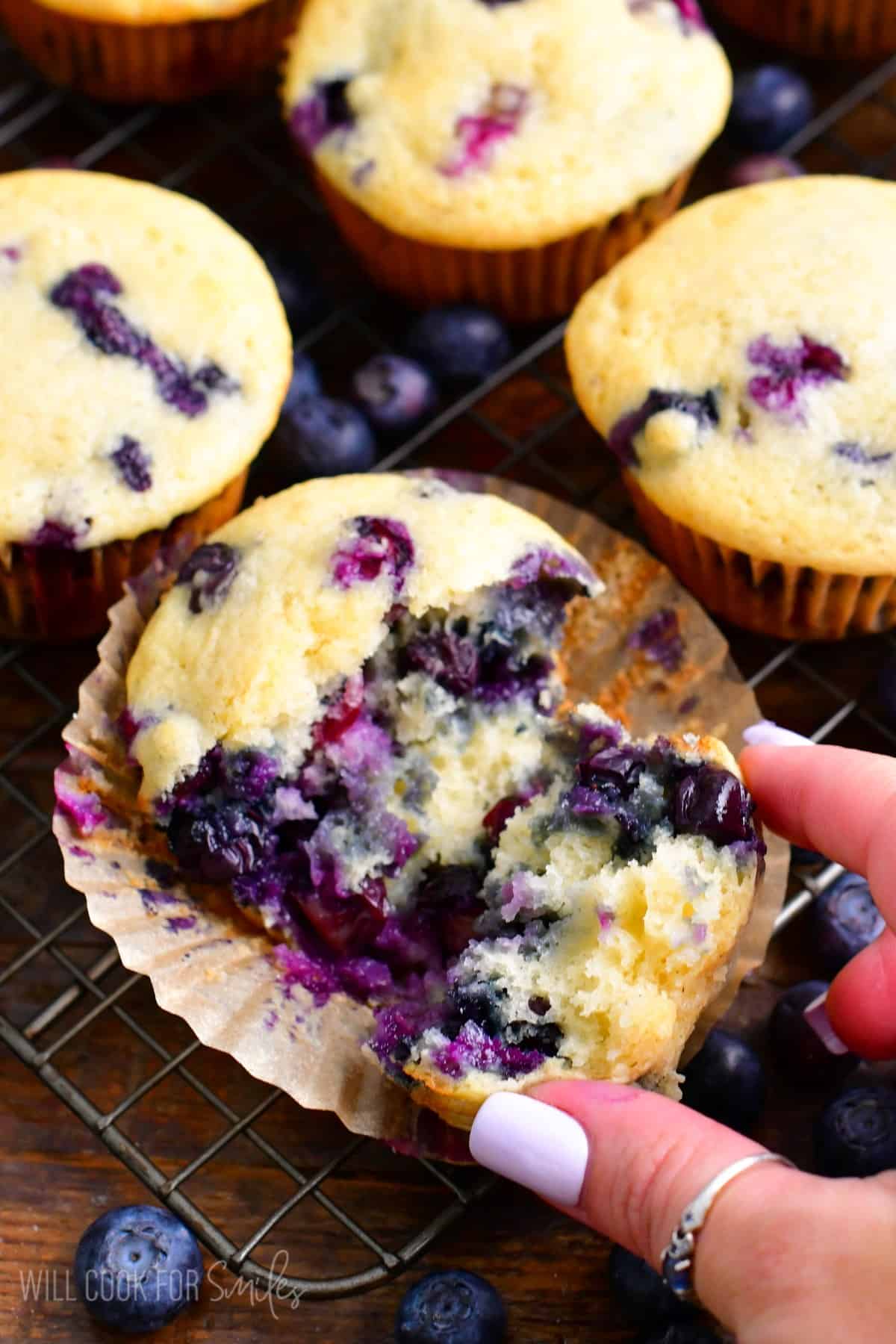 Blueberry muffins on a wire wrack with one of them broken in half.