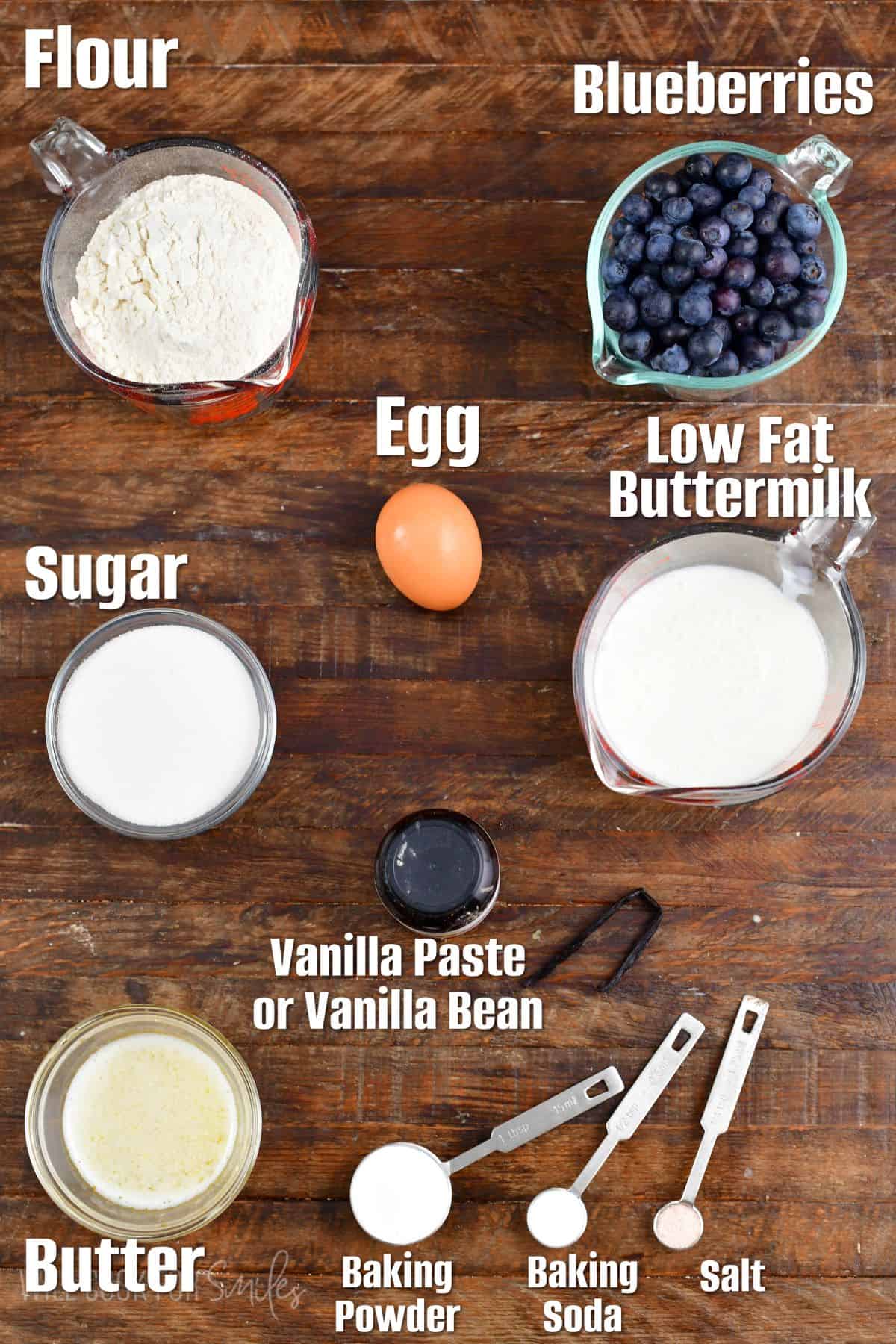 Labeled ingredients for blueberry muffins on a wood surface.