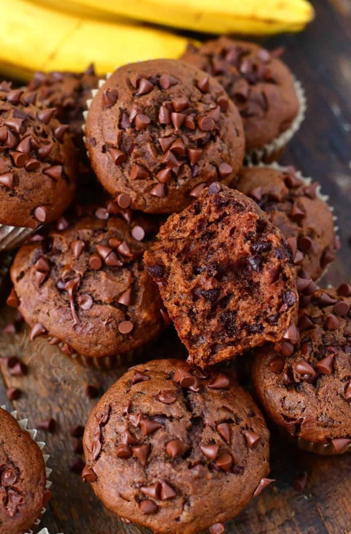 several chocolate muffins on wooden board one broken in half to see inside.