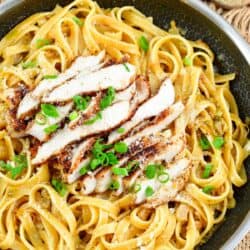lemon Pepper chicken over pasta in a pan with green onions on top as garnish.