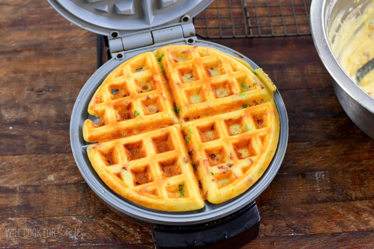 Cooked savory waffle in a waffle maker that is opened up and on a wood surface.